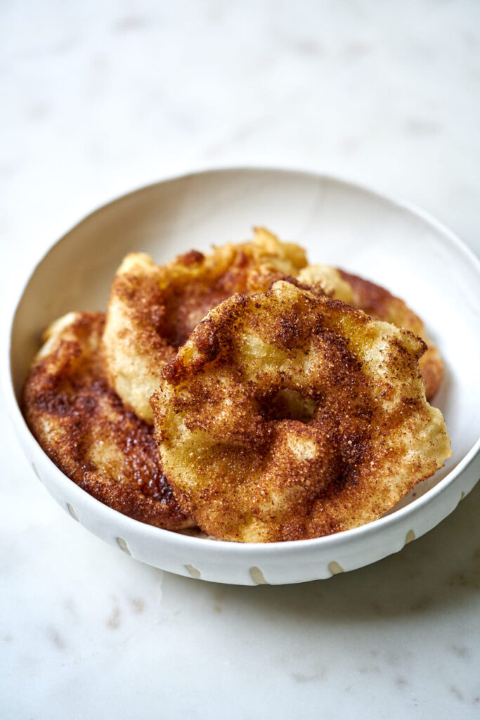 White plate full of fried apple slices covered in cinnamon sugar.