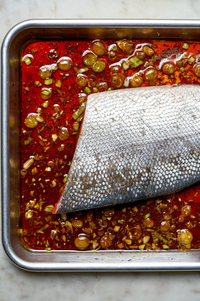 A piece of salmon skin side up in a baking sheet with teriyaki style sauce.