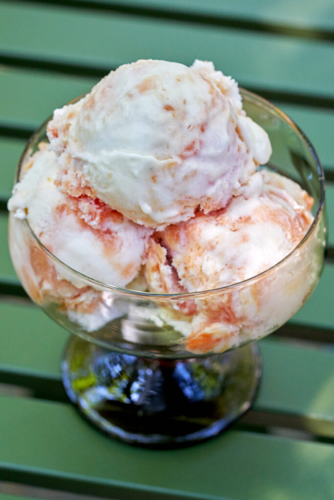 Three scoops of nectarine semifreddo in a pedestal glass on a green table.