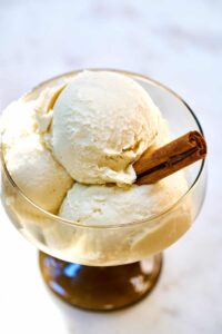 Three scoops of ice cream in a pedestal glass with a stick of cinnamon.