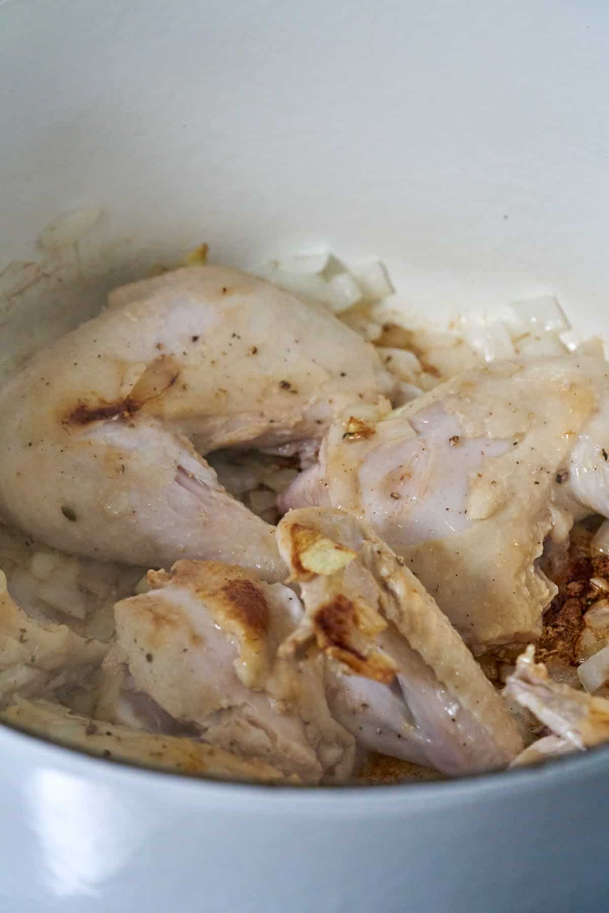 Browned chicken in a pot with onions.