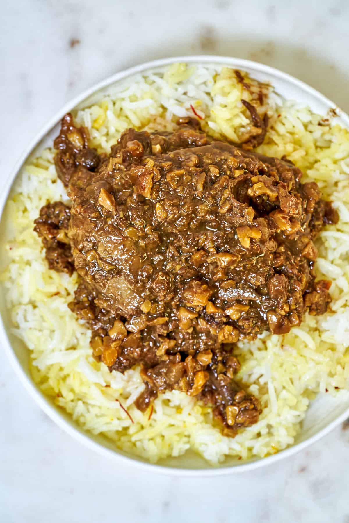 Top view of walnut and chicken stew over rice in a white plate.