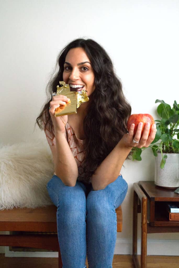 Woman eating a chocolate bar and holding an apple.