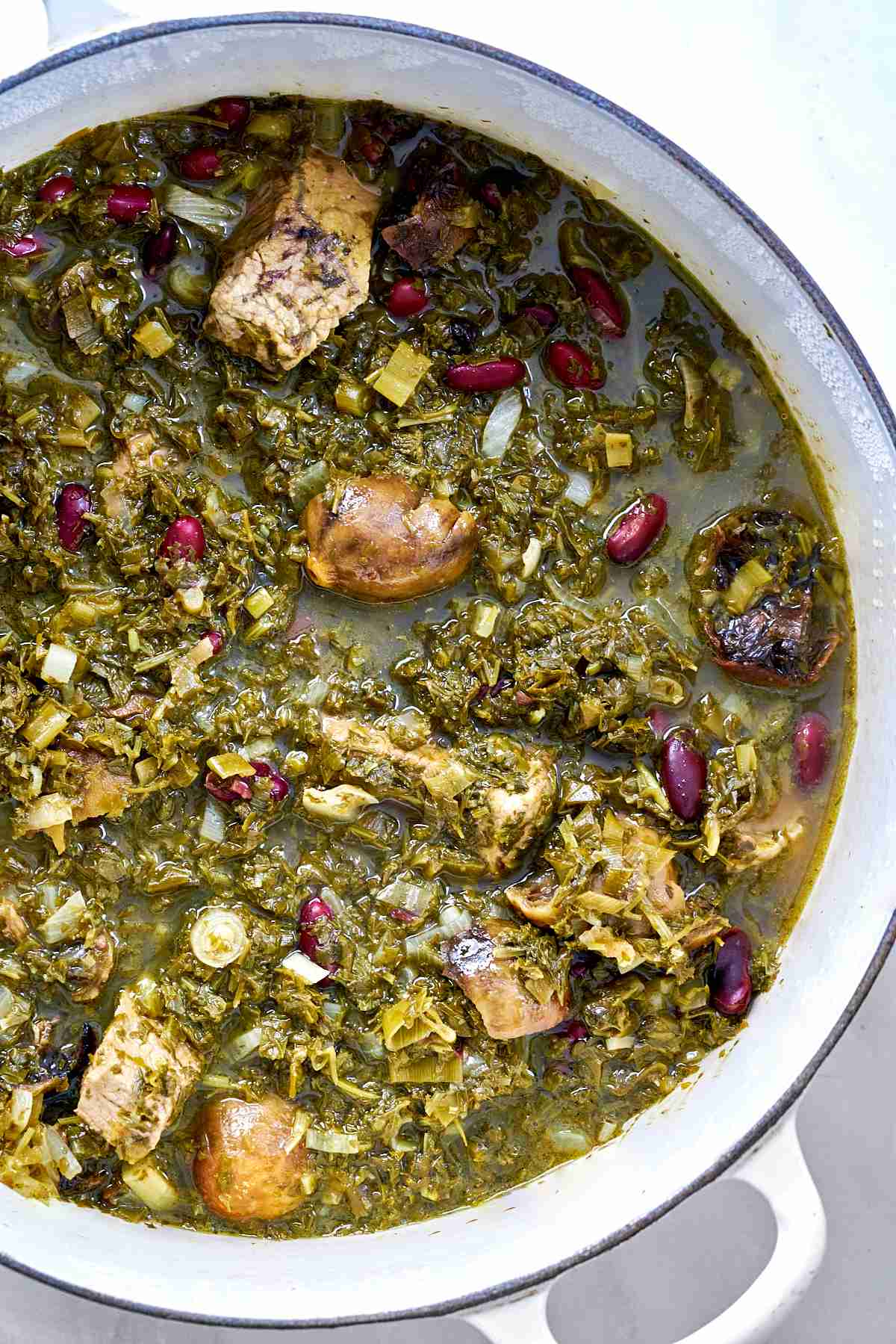 Top view of a green stew with beef, herbs, and kidney beans.