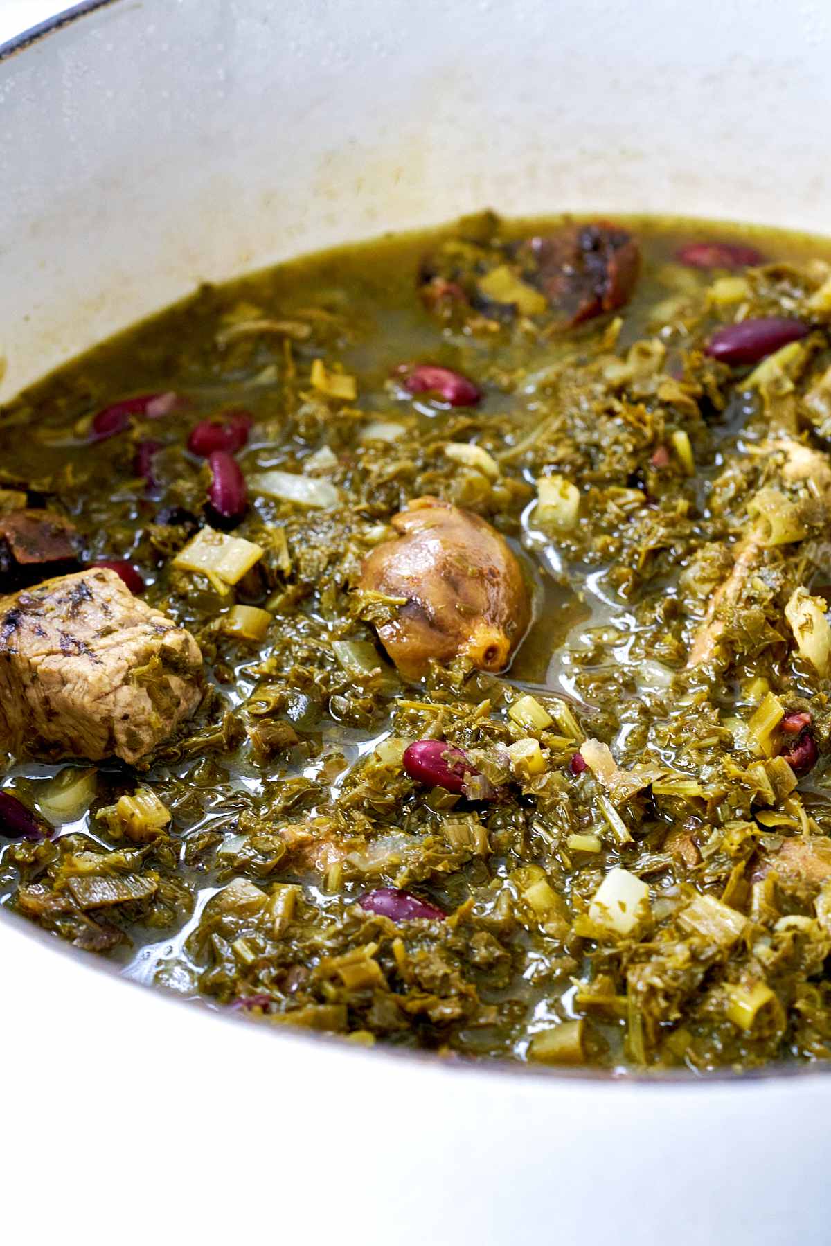 Close up of a green stew with cubes of beef and dried limes in a big pot.