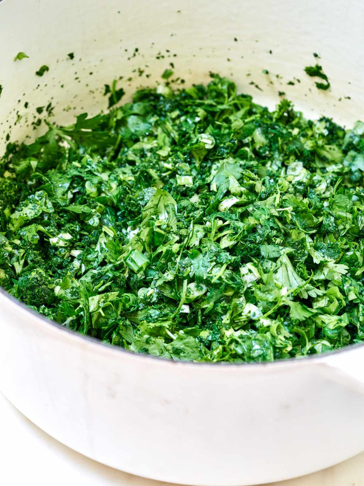 Chopped greens wilting as they cook in a white pot.