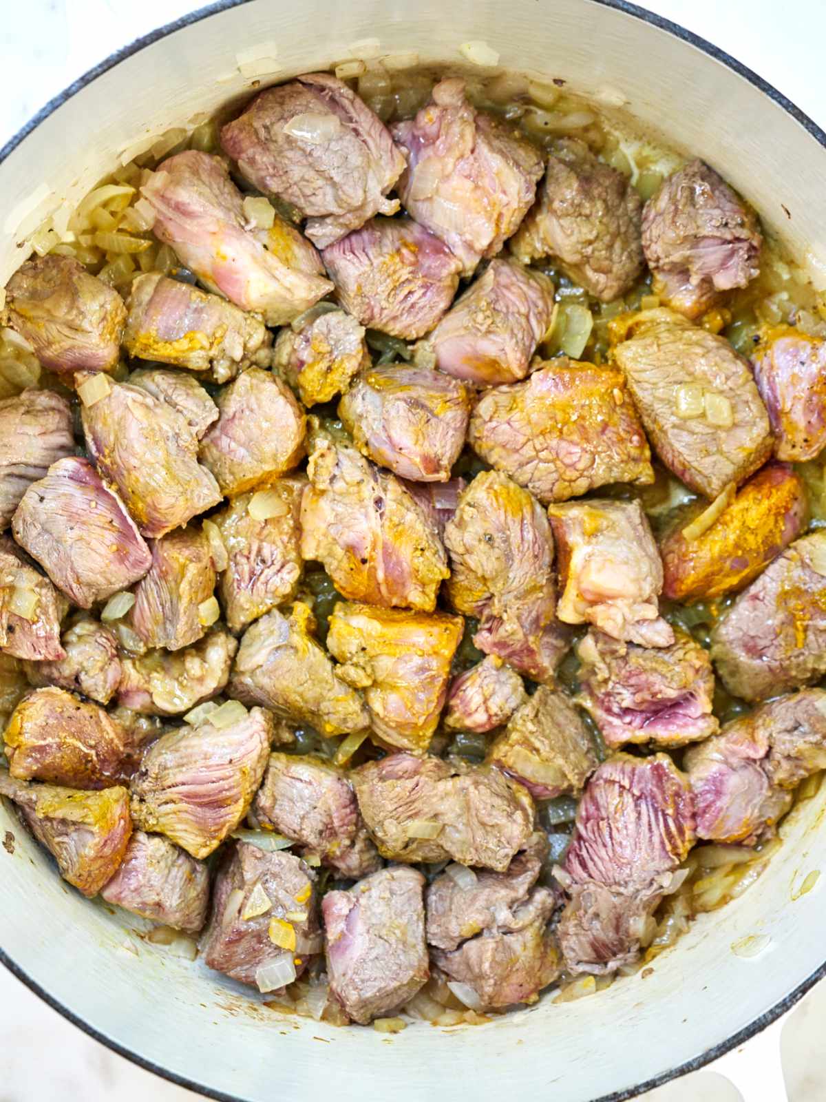 Browned stew meat in a large white pot.