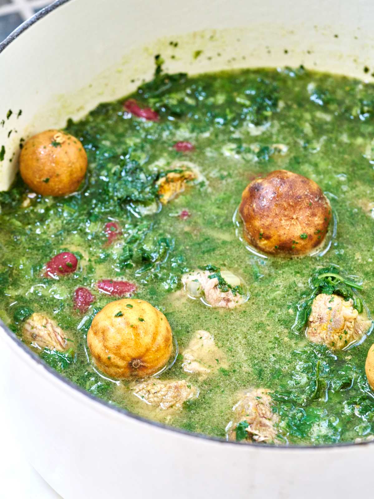 Green stew with dried limes on top in a large, white pot.