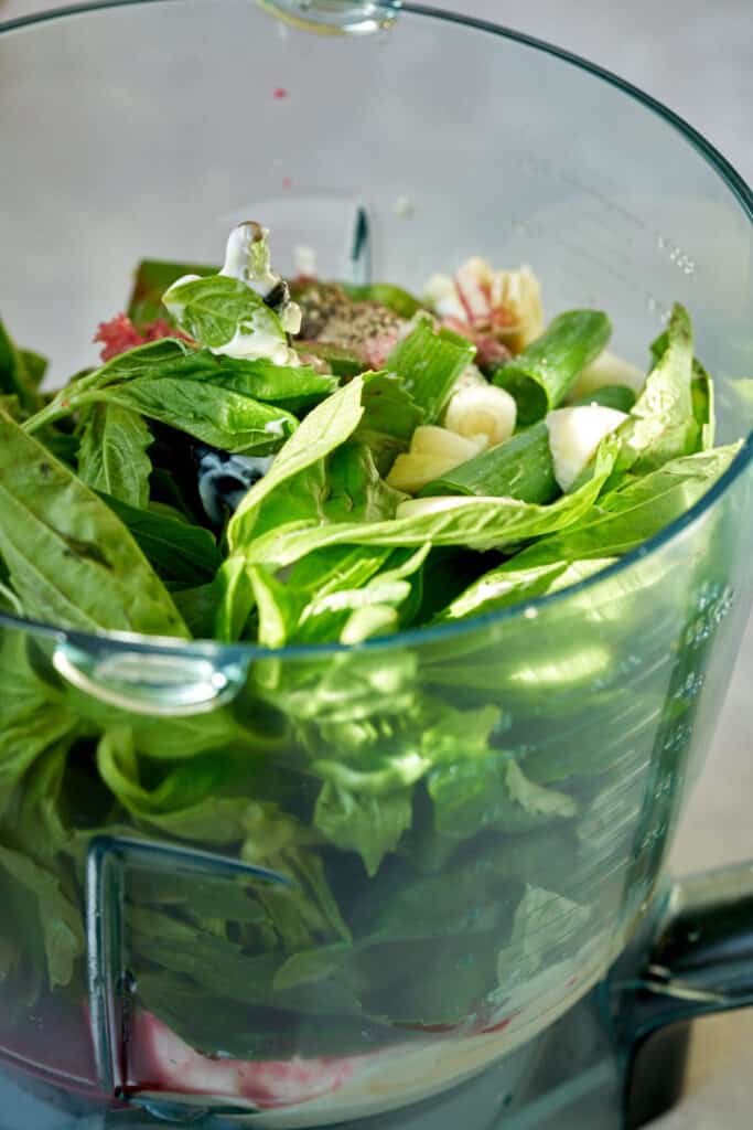 Food processor full of herbs and othe salad dressing ingredients.