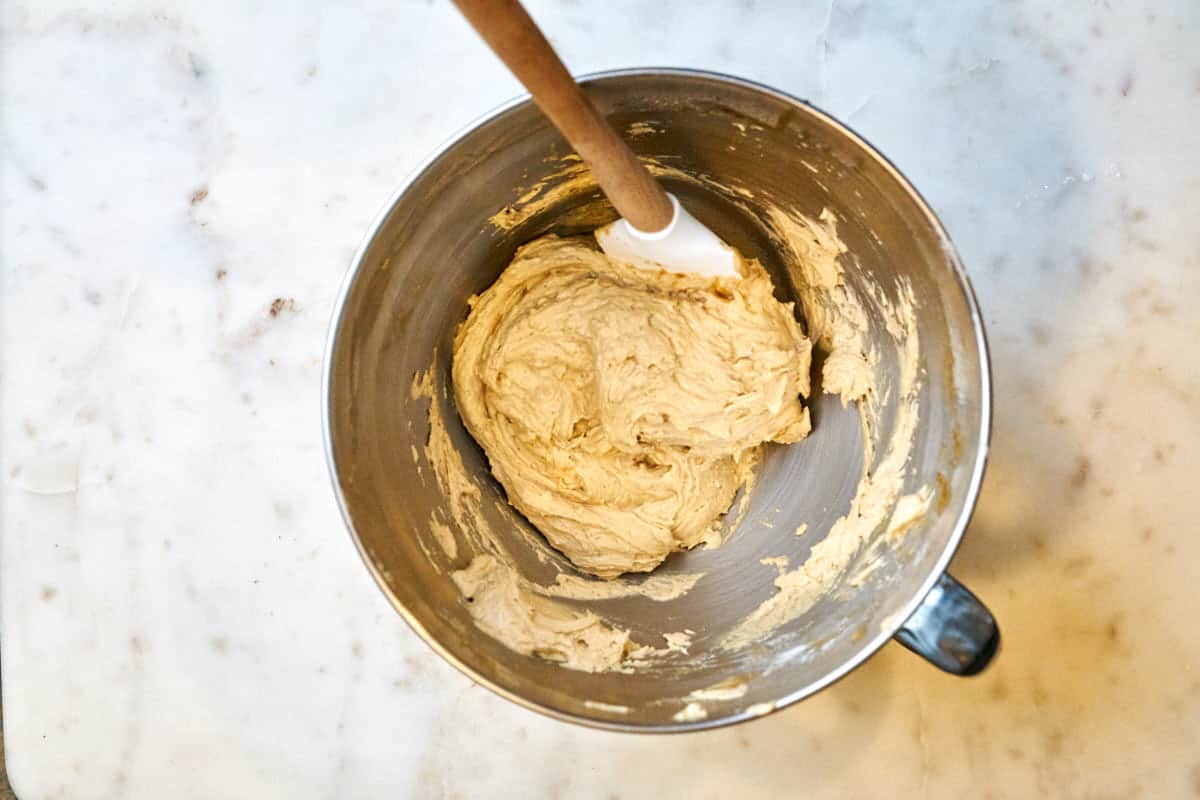 Cookie batter in a stand mixer bowl with a rubber spatula.