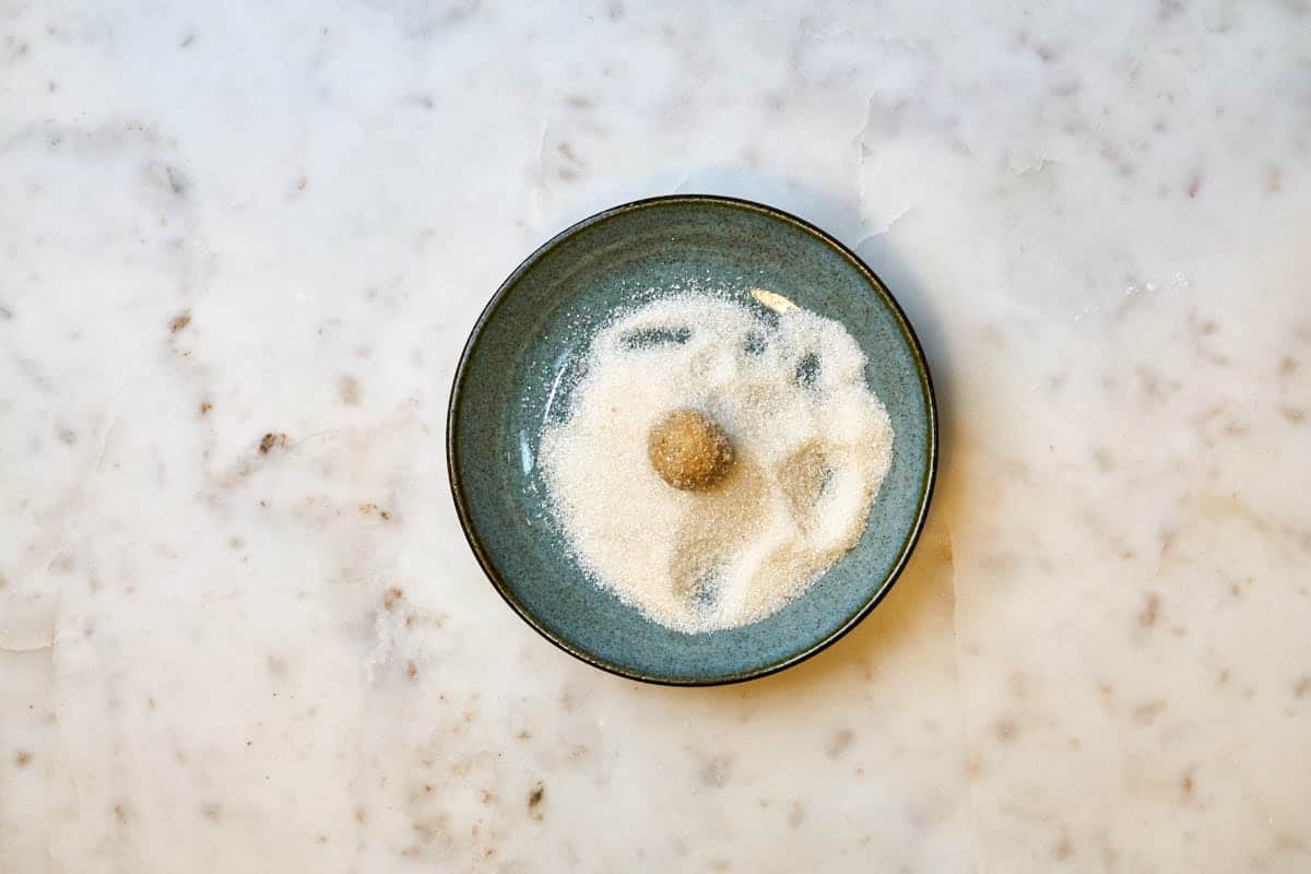 One ball of cookie dough in a plate filled with sugar.