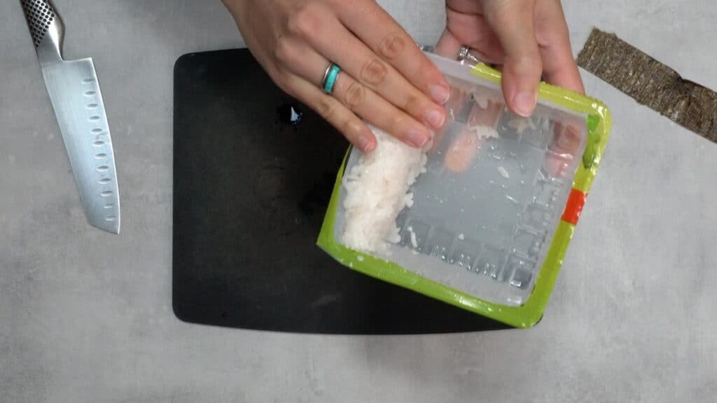 Pressing rice into the side of a tofu container.