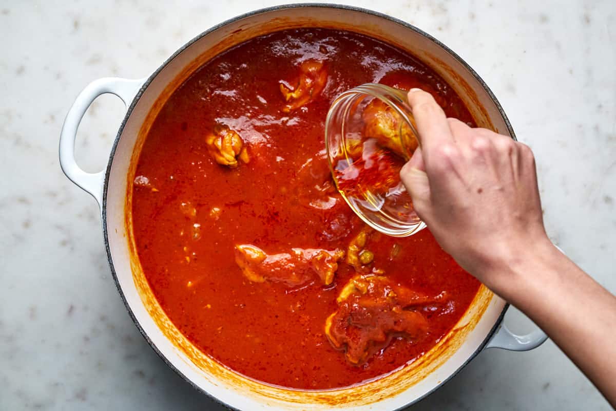 Hand pouring steeped saffron into pot of red stew.