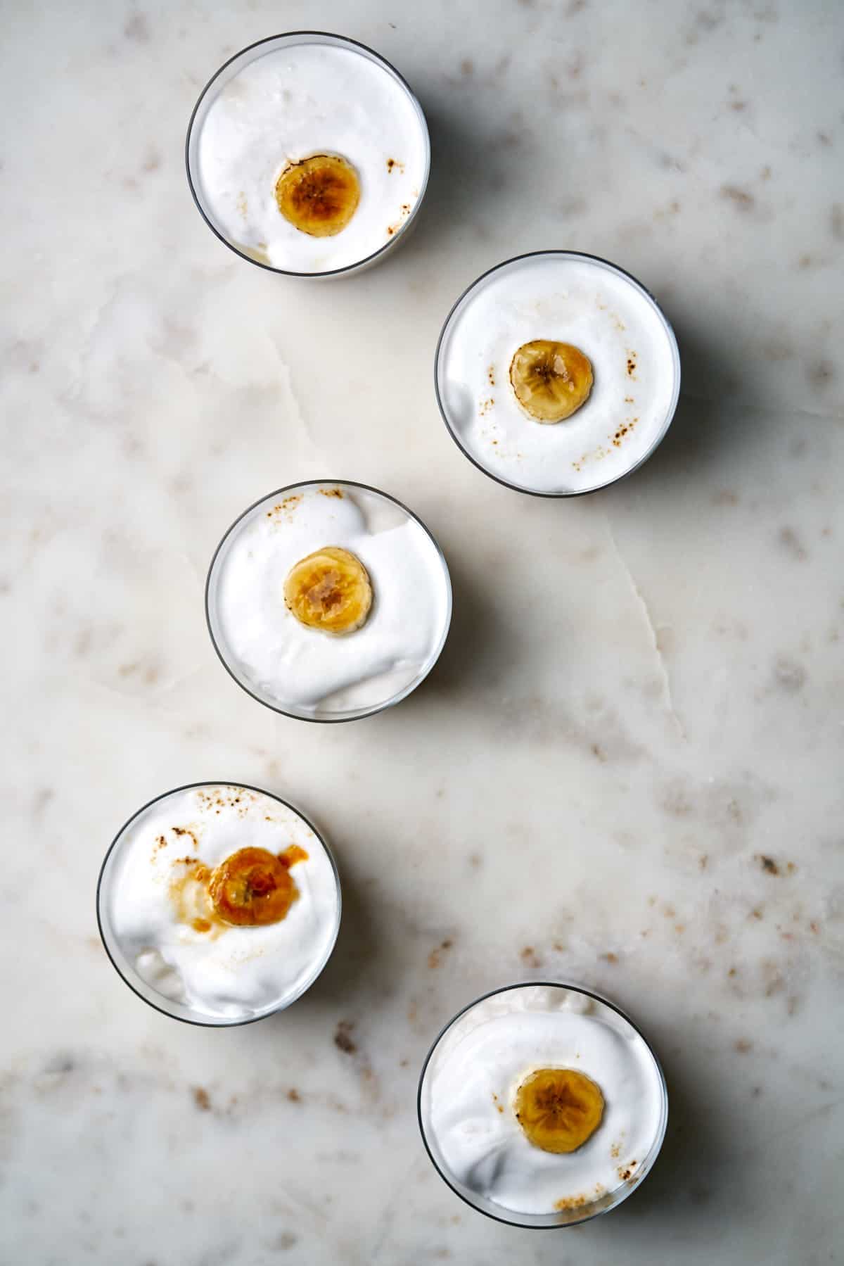 Top view of five banana cream pie cups filled with whipped cream and topped with a bruleed banana slice.