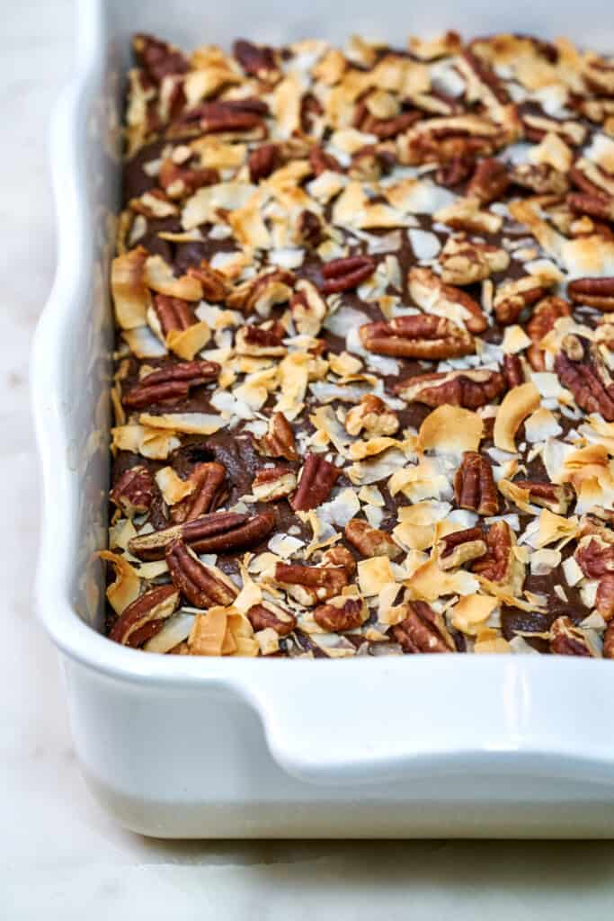 Cake in a white baking dish covered in pecans and coconut after baking.