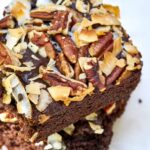 Two pieces of chocolate cake with coconut and nuts stacked on top of each other.