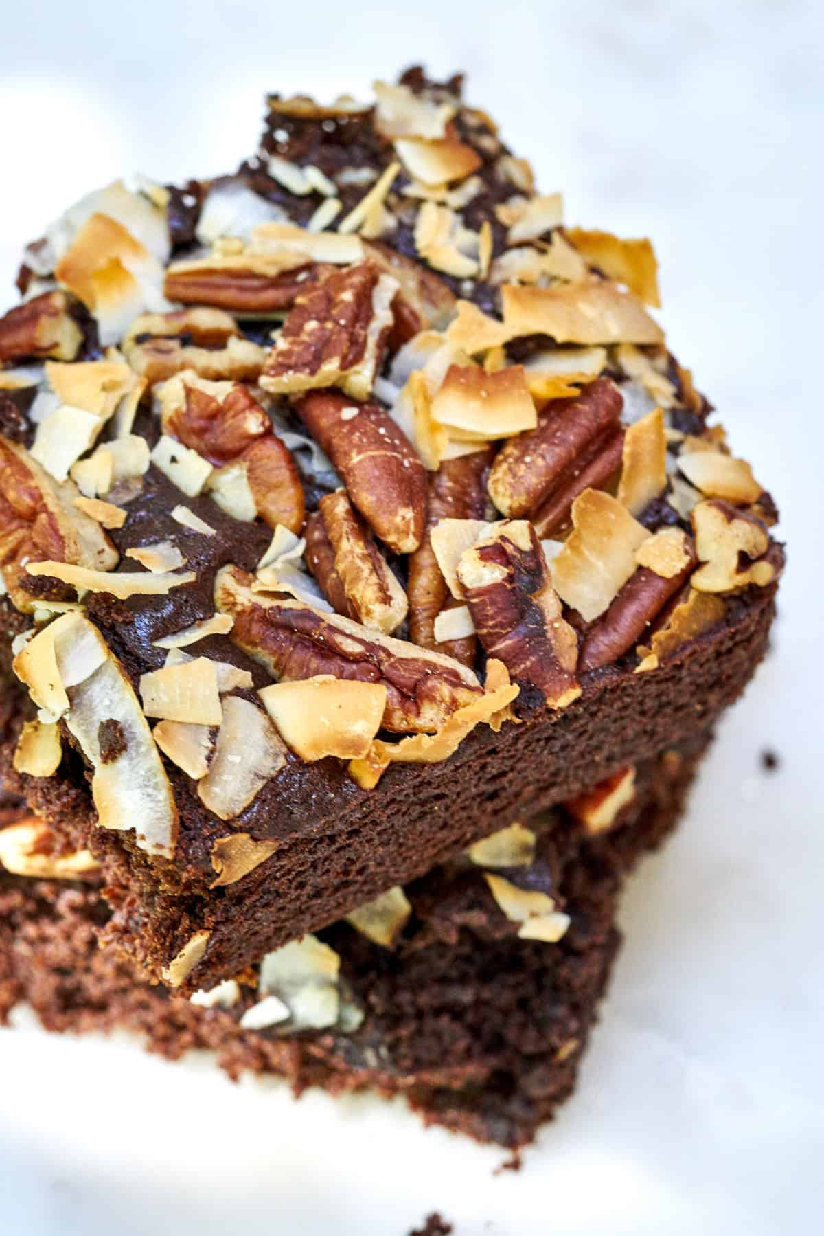 Two pieces of chocolate cake with coconut and nuts stacked on top of each other.