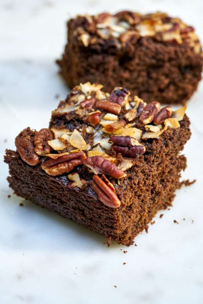 Two slices of brown cake topped with nuts and coconut.