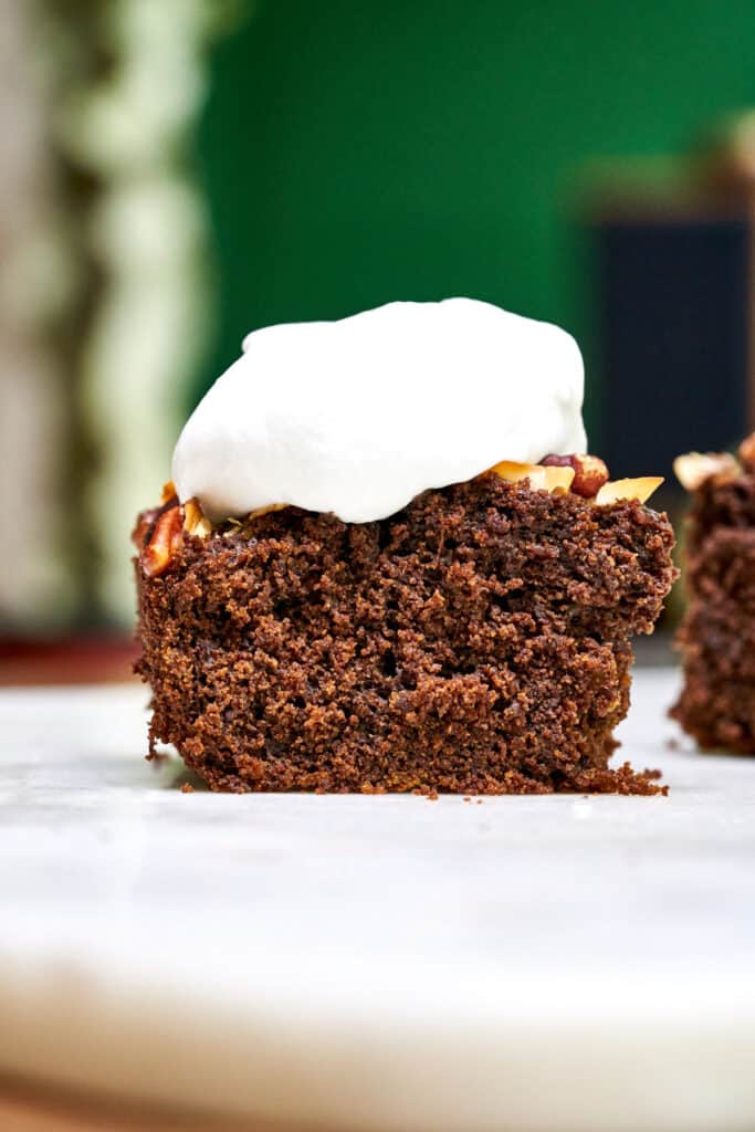 Front view of one piece of cake topped with whipped cream on a white table with green background.