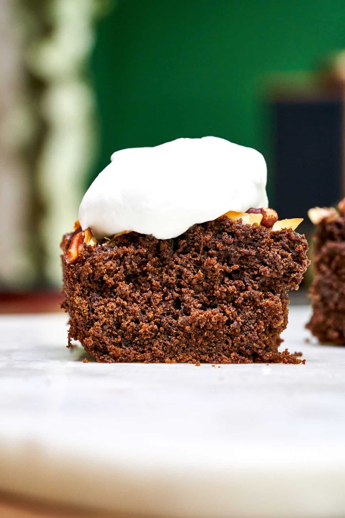 A slice of chocolate ginger cake with nuts and whipped cream on top.