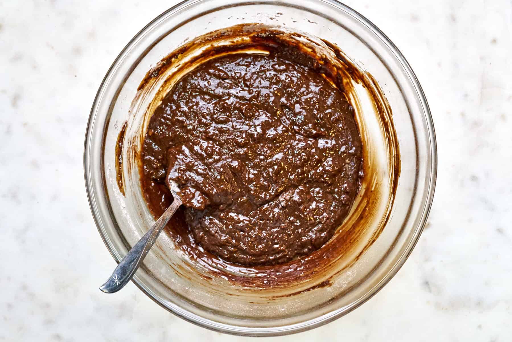 Wet cake batter in a glass bowl with a metal spoon.