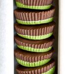 Stack of peanut butter cups that have green bottoms and chocolate tops.