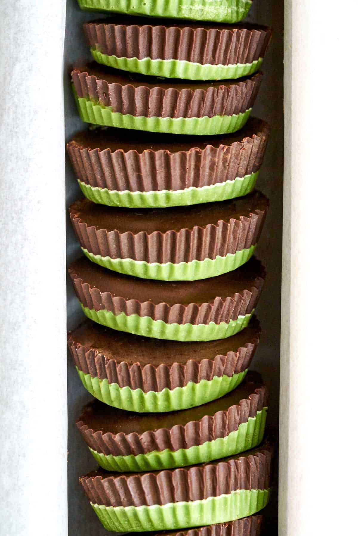 Stack of peanut butter cups that have green bottoms and chocolate tops.