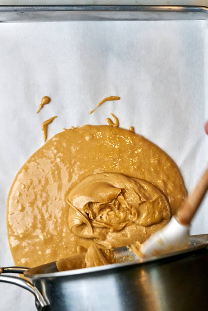 Pouring toffee from a saucepan onto a sheet pan.