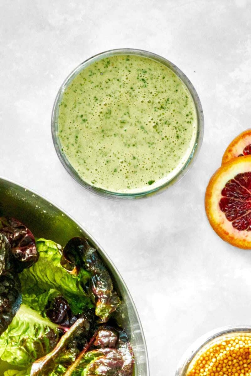 Salad dressing next to lettuce and a sliced orange.