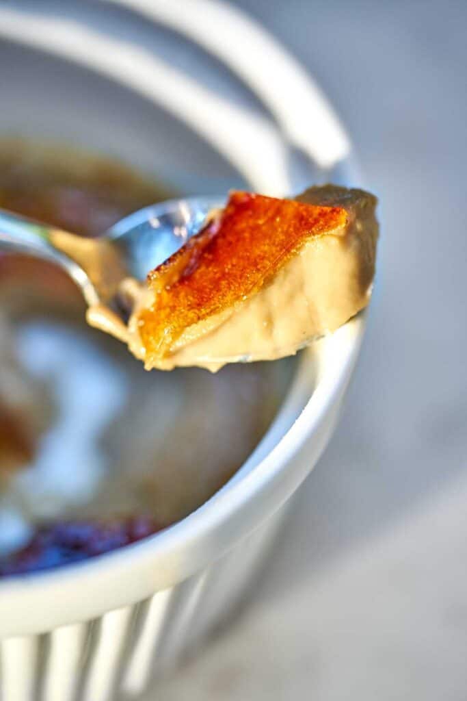 Spoon with custard and creme brulee sugar topping leaning on a ramekin.