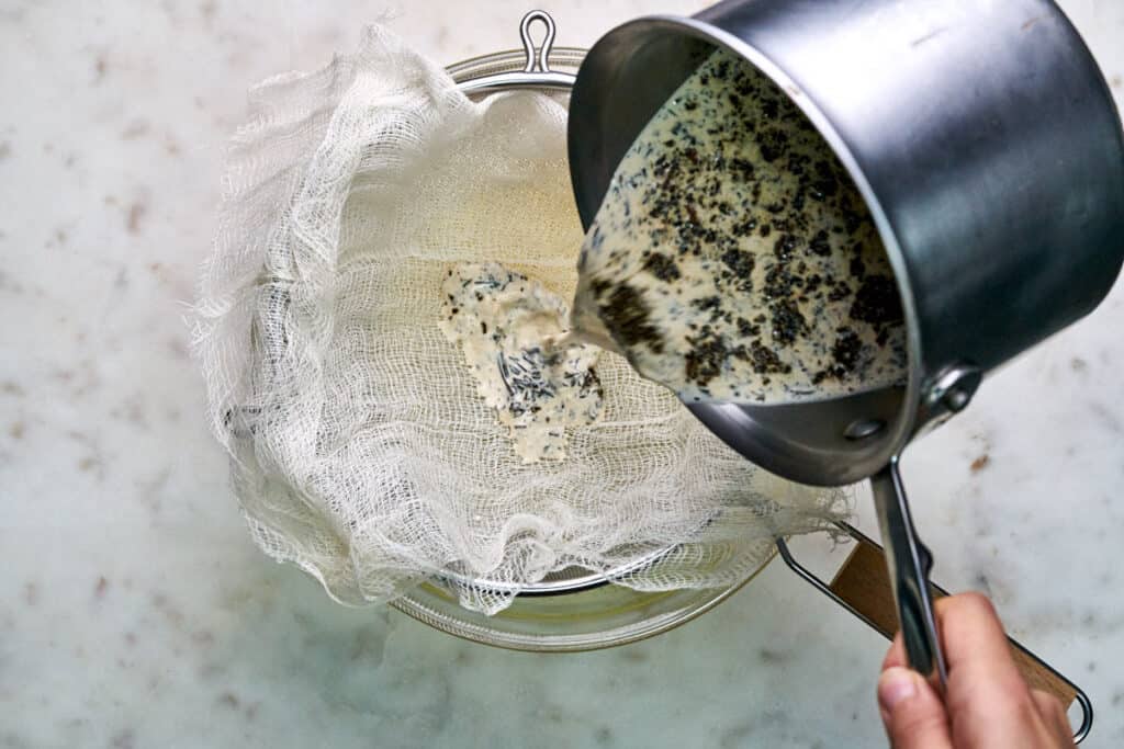 Pouring tea and cream through a strainer lined with cheesecloth.