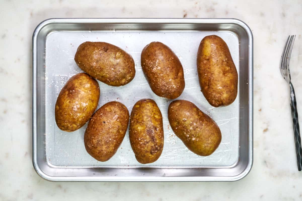 Seven potatoes on a quarter baking sheet next to a fork.