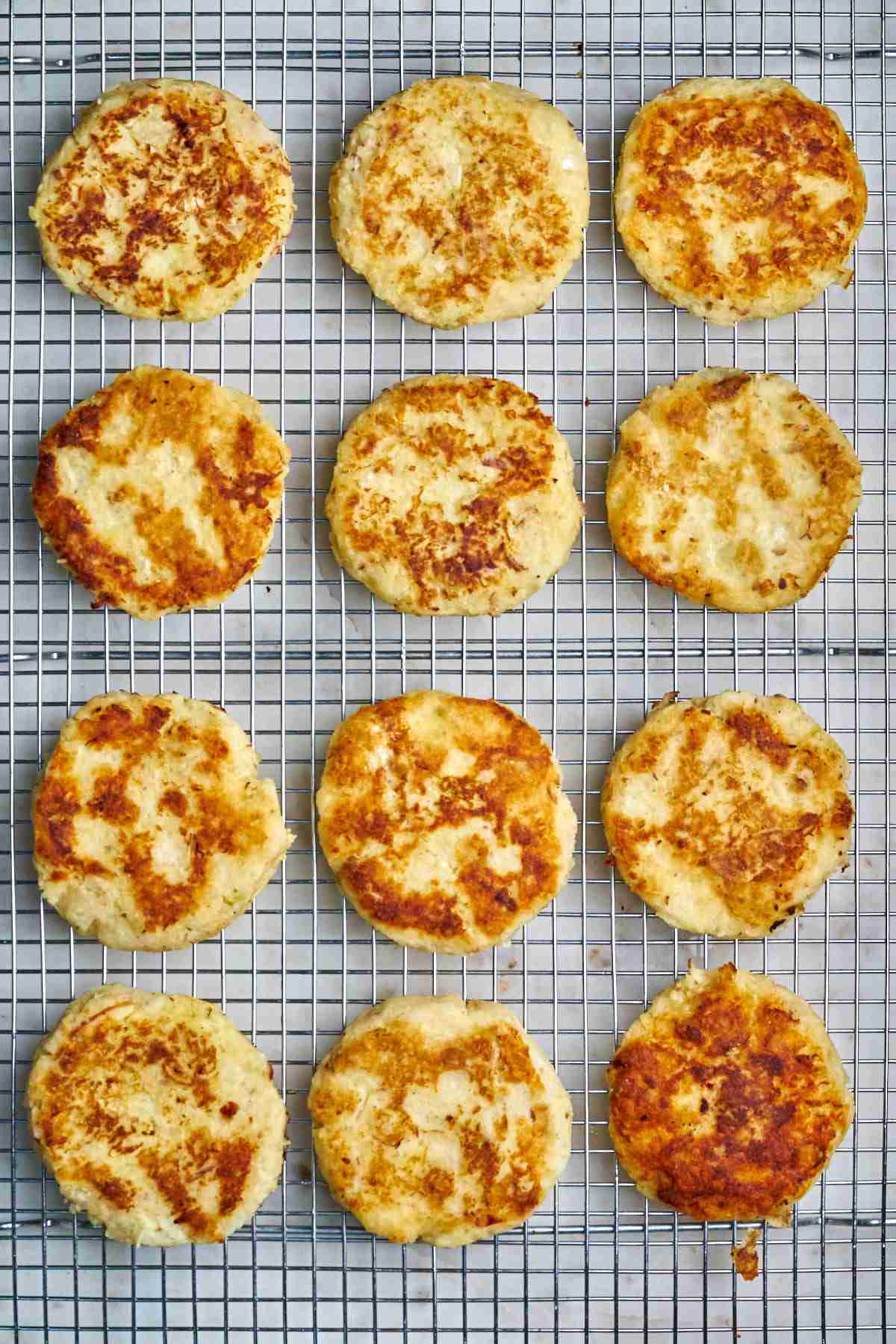 Twelve cooked latkes on a wire rack.