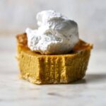 Front view of a slice of pumpkin pie with whipped cream on top.