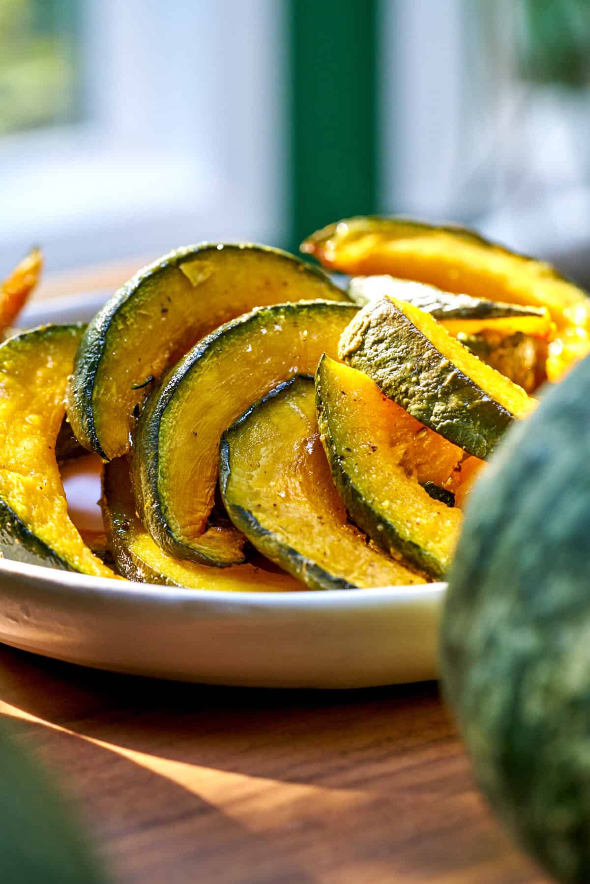 Roasted kabocha squash on a white plate on a wood table.