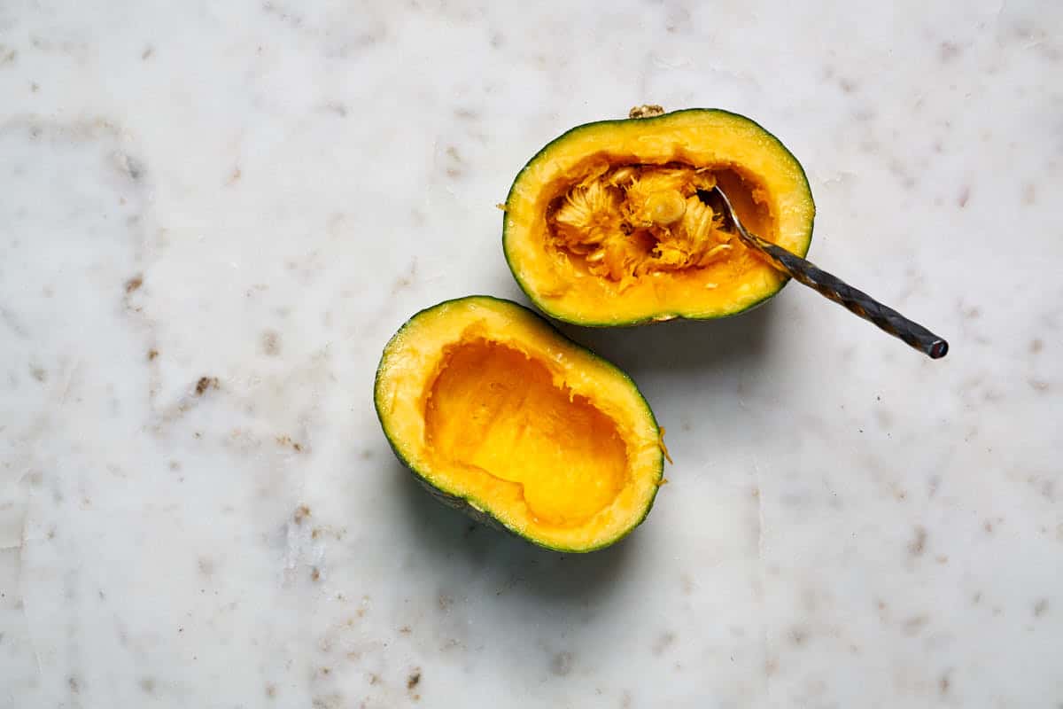 One kabocha squash cut in half with half the seeds scooped out and a spoon.