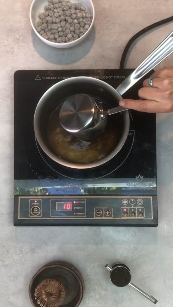 A hand pouring a white bowl of tapioca pearls over a saucepan of boiling water.