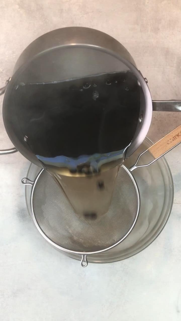 Boba and water being poured into a glass dish with a metal strainer.