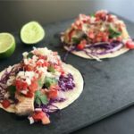 Two tacos on a cutting board.