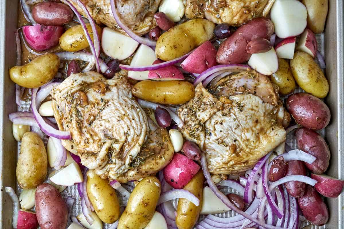 Raw chicken on a baking sheet with potatoes.