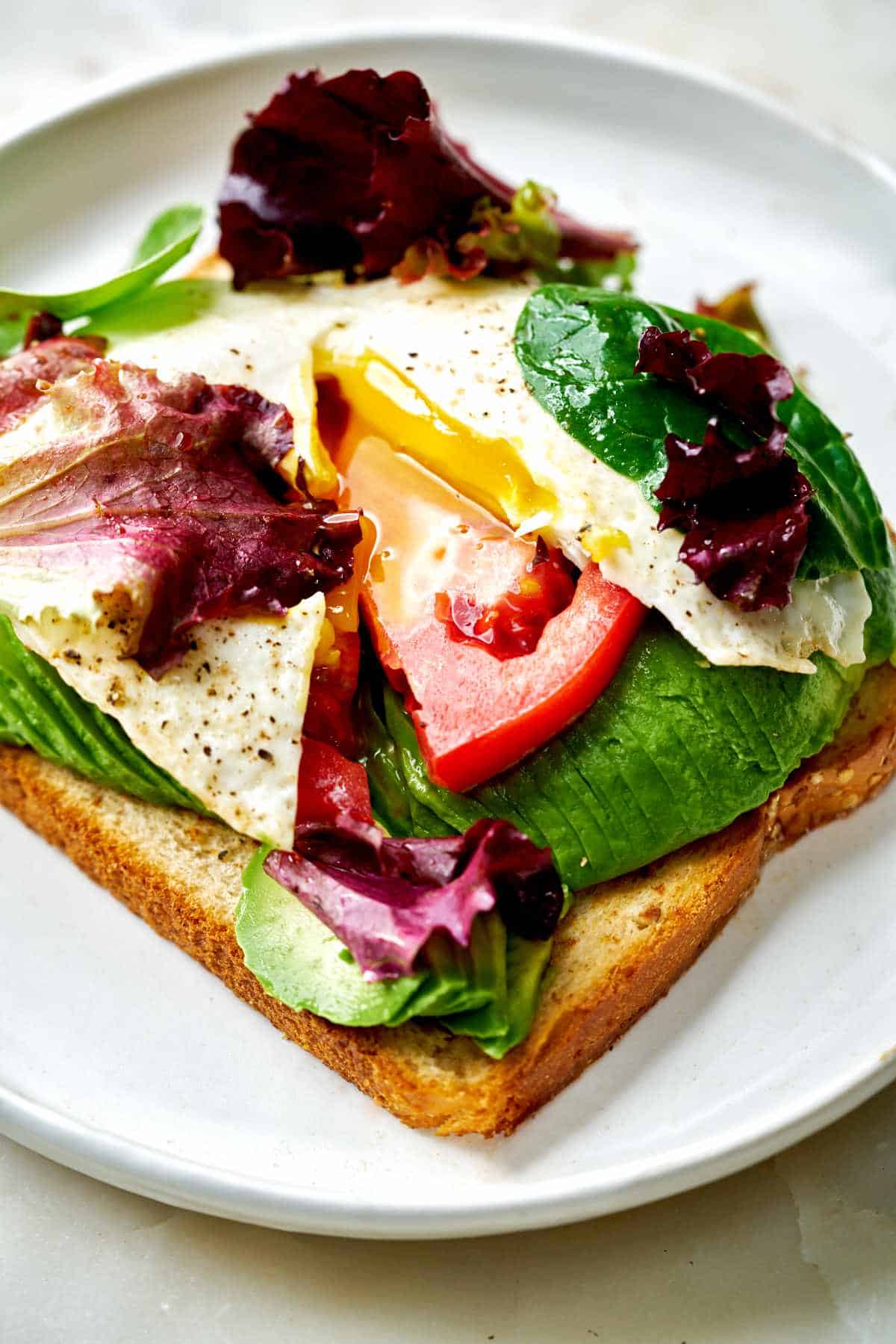 Close up of toast topped with avocado, eggs, and lettuce.