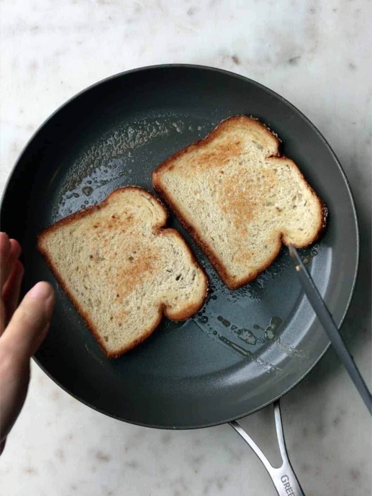 Toast in a non-stick pan with a hand flipping one piece of bread with a spatula..