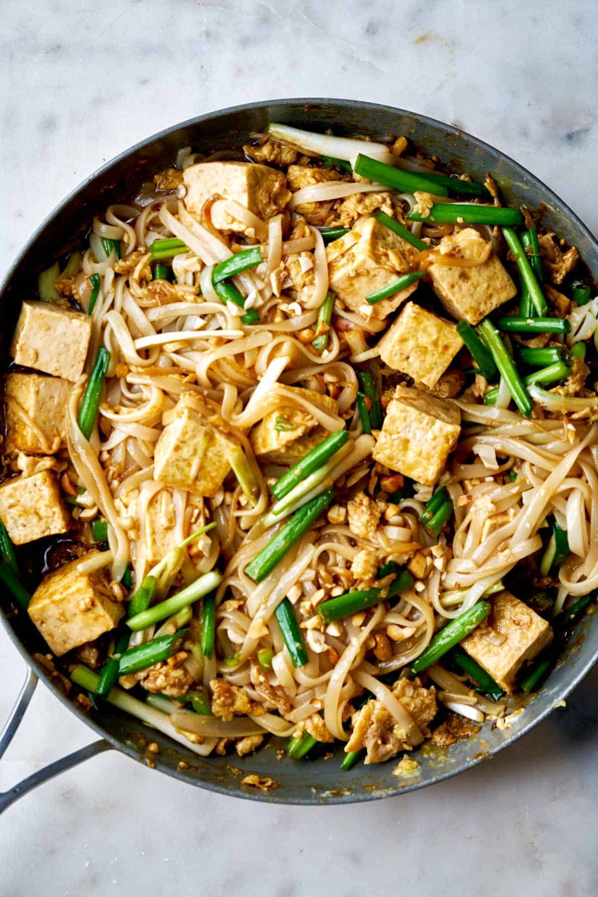 Noodles and tofu in a fry pan.