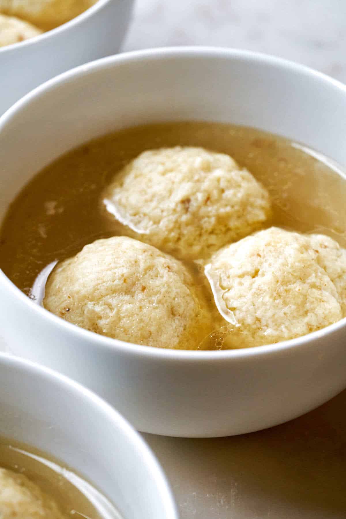 Matzo ball soup in three white bowls.