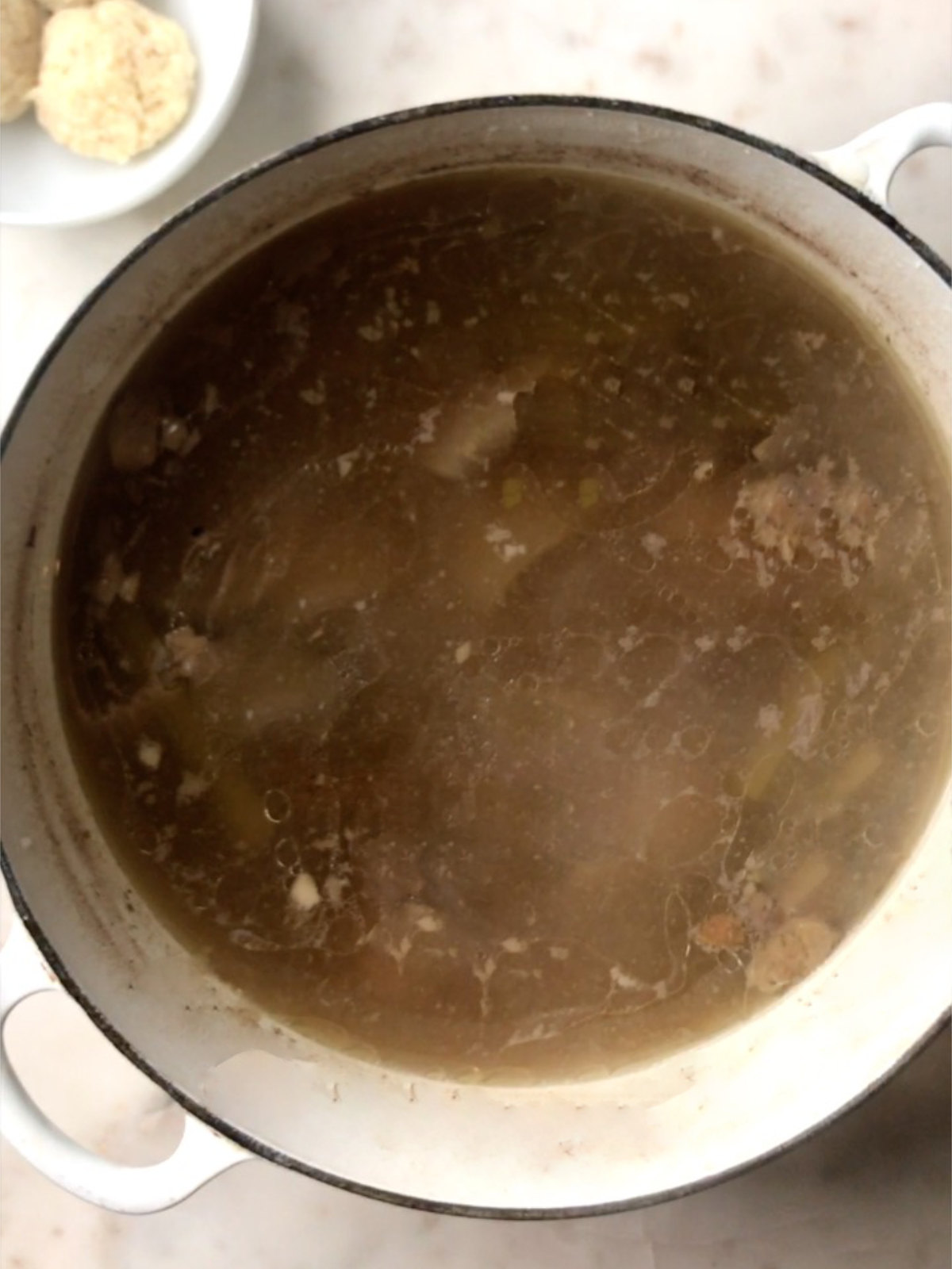 Large pot of chicken stock next to matzo balls in a small bowl.