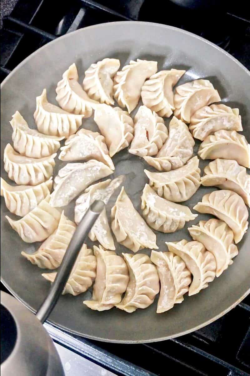 Pouring water into a pan to steam dumplings.