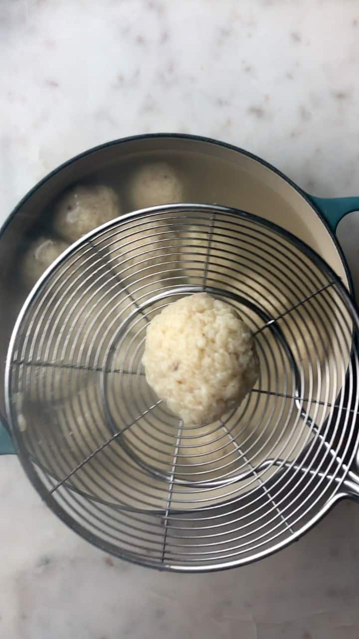 Spider spatula with a matzo ball over a pot of matzo balls.