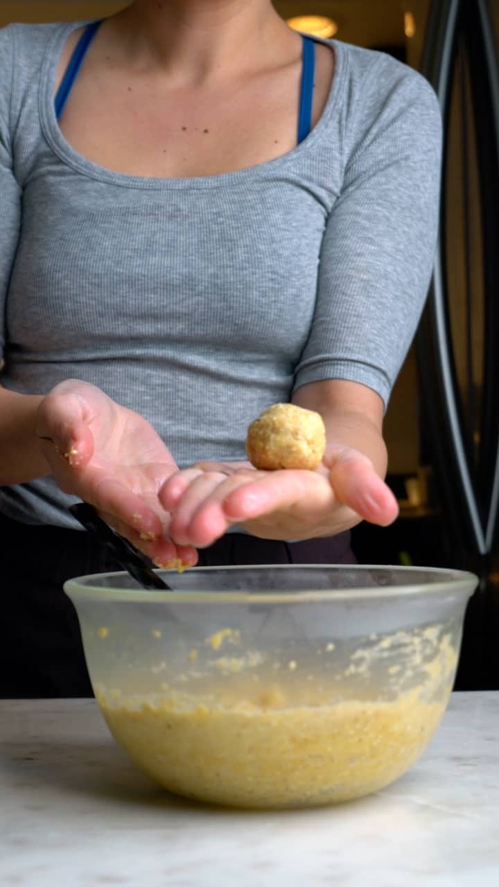 Matzo ball on a hand over a glass bowl with matzo ball mixture.