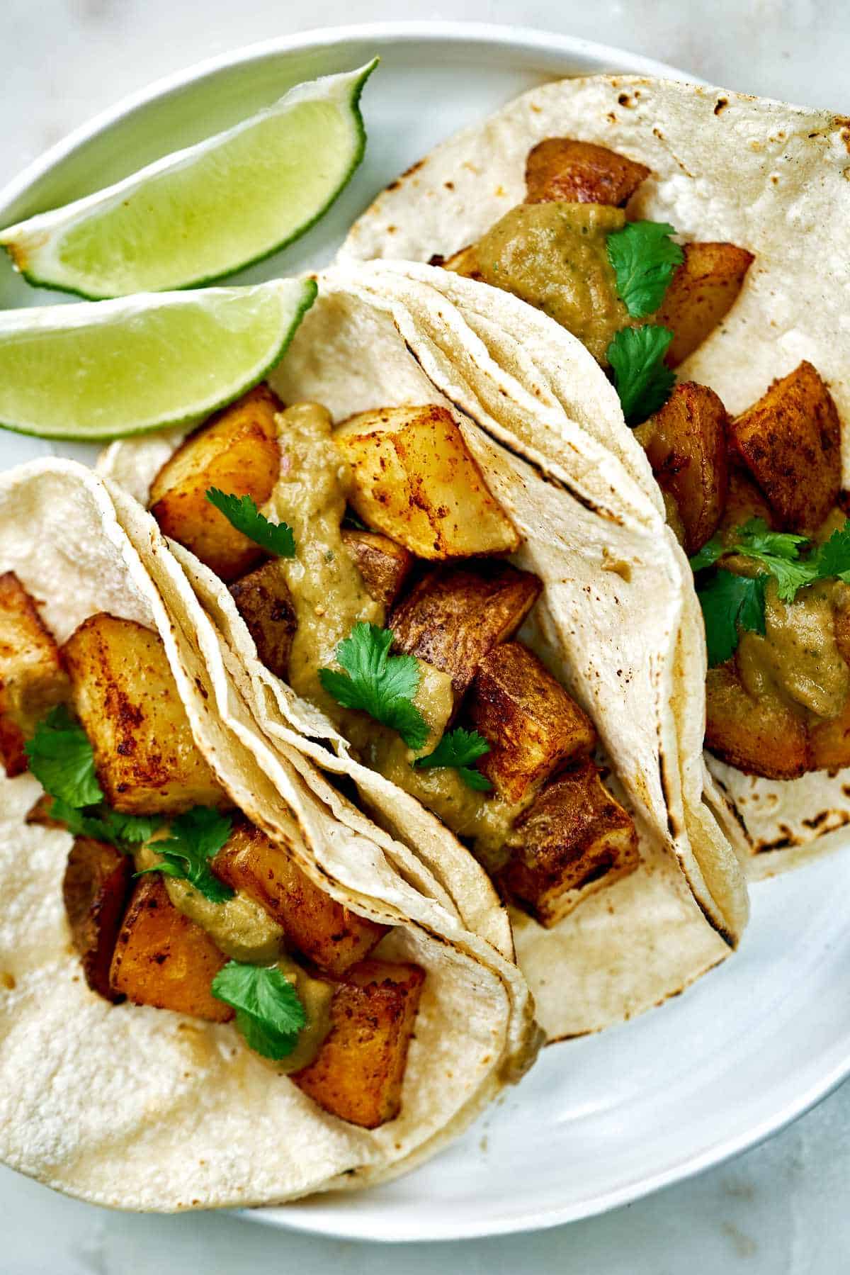 A plate with three tacos and lime wedges.