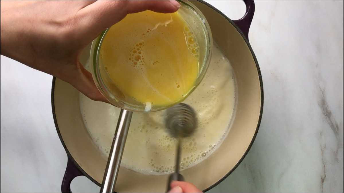 Pouring eggs into milk in a pot.